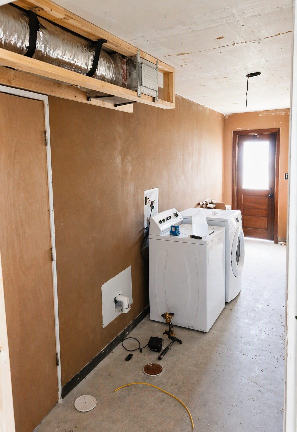Same laundry room before renovation, showing bare drywall and subfloor